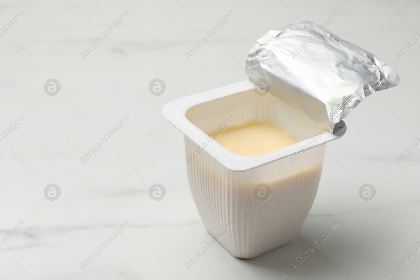 Photo of Delicious yogurt in plastic cup on white marble table, closeup. Space for text