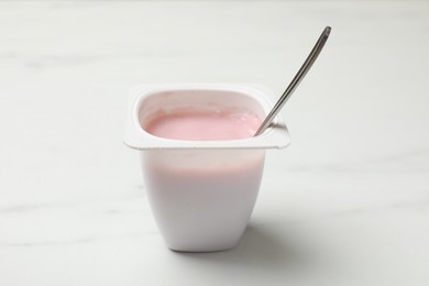 Photo of Delicious yogurt in plastic cup with spoon on white marble table, closeup