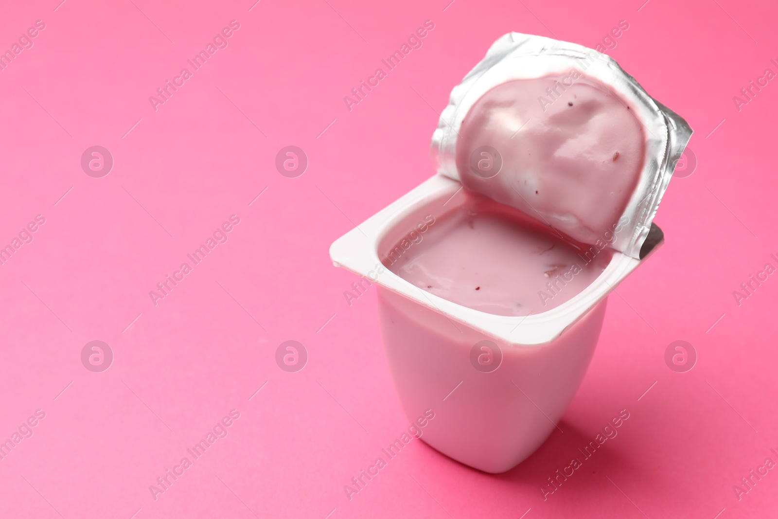 Photo of Delicious yogurt in plastic cup on pink background, closeup. Space for text