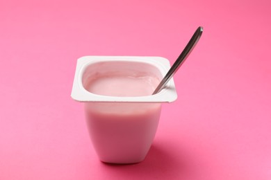 Photo of Delicious yogurt in plastic cup with spoon on pink background, closeup