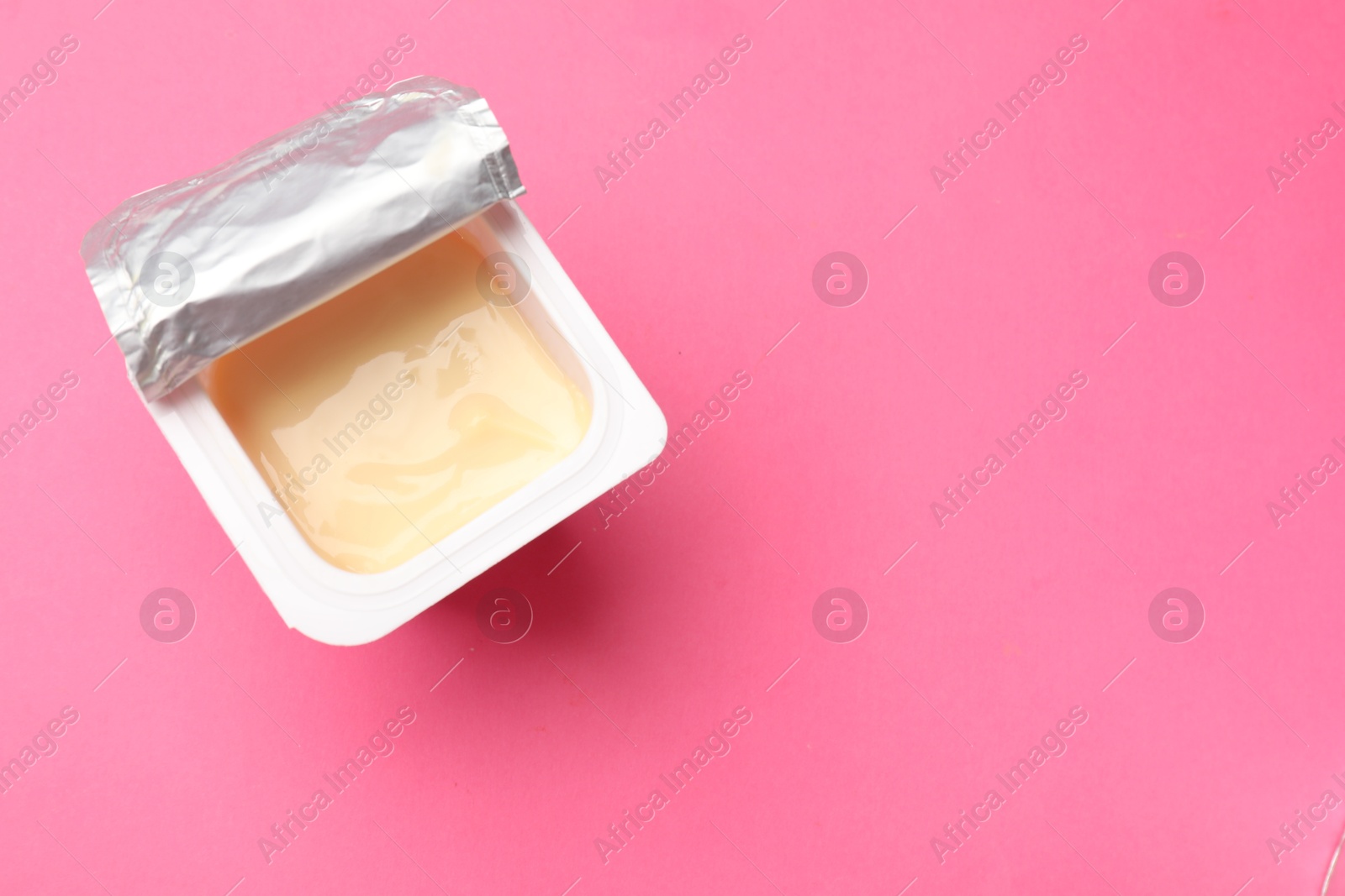 Photo of Delicious yogurt in plastic cup on pink background, top view. Space for text