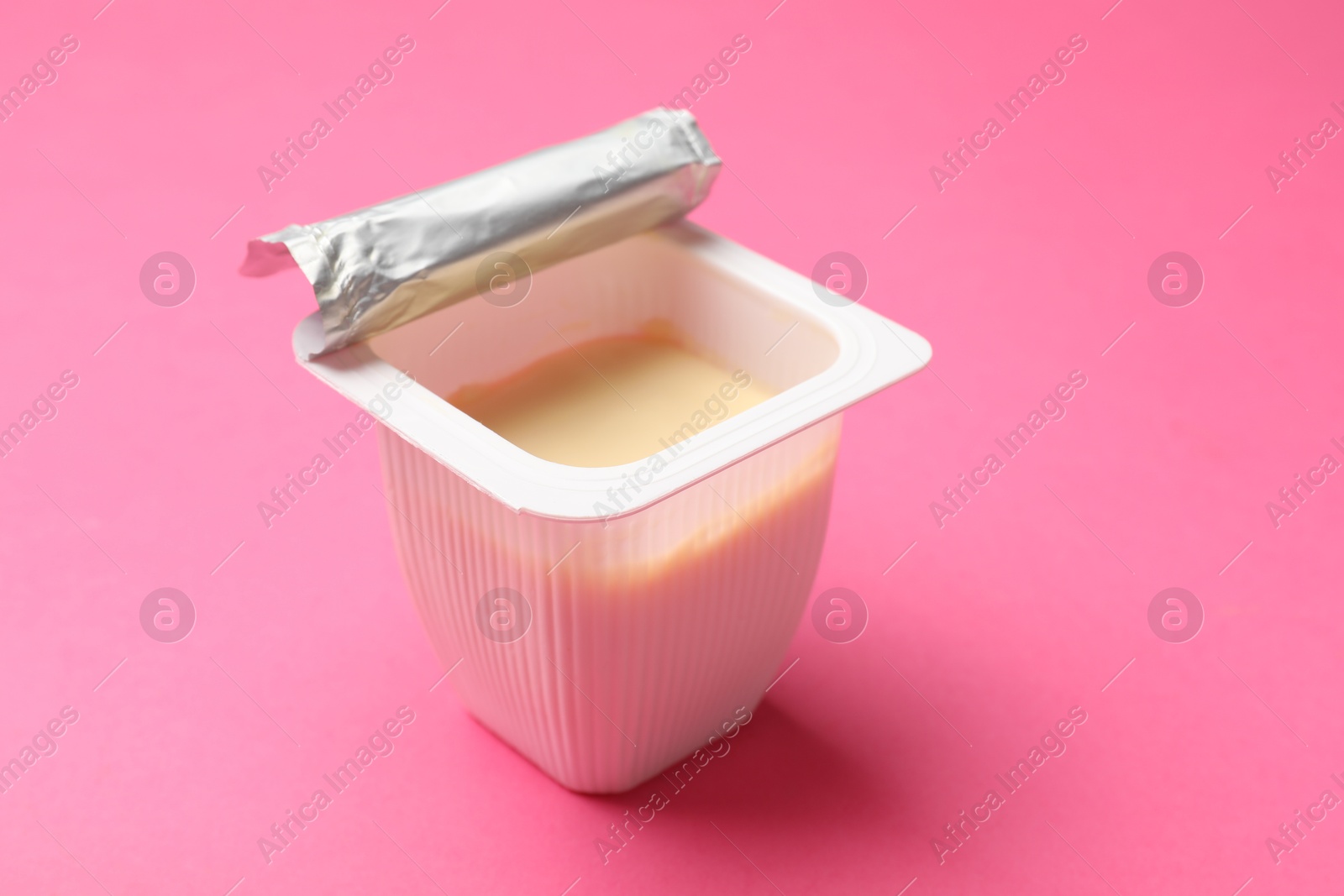 Photo of Delicious yogurt in plastic cup on pink background, closeup