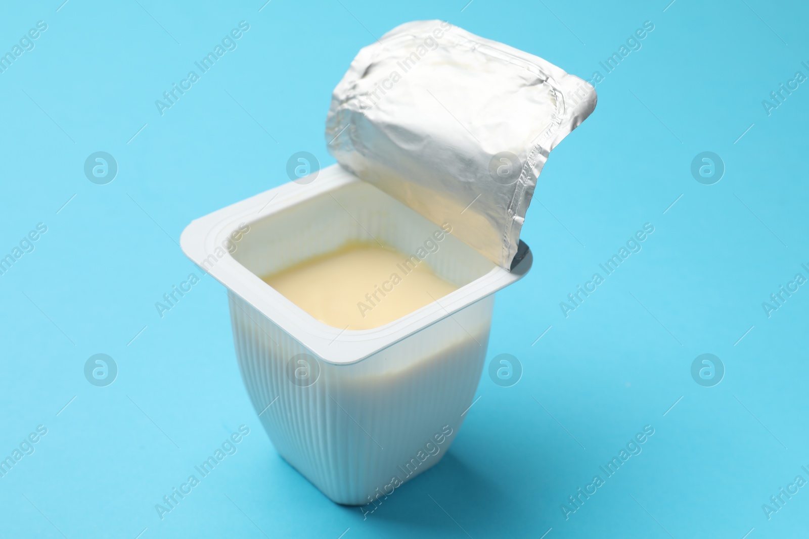 Photo of Delicious chocolate yogurt in plastic cup on light blue background, closeup