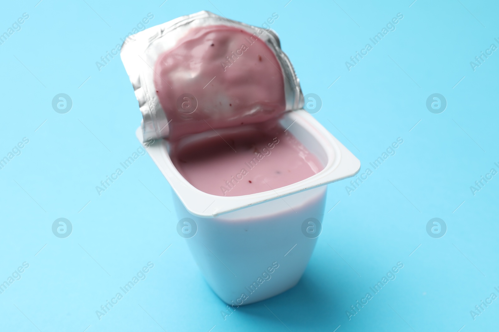 Photo of Delicious chocolate yogurt in plastic cup on light blue background, closeup