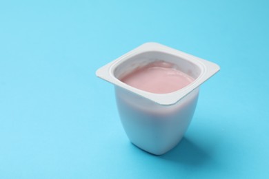 Photo of Delicious chocolate yogurt in plastic cup on light blue background, closeup. Space for text