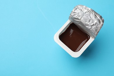 Photo of Delicious chocolate yogurt in plastic cup on light blue background, top view. Space for text