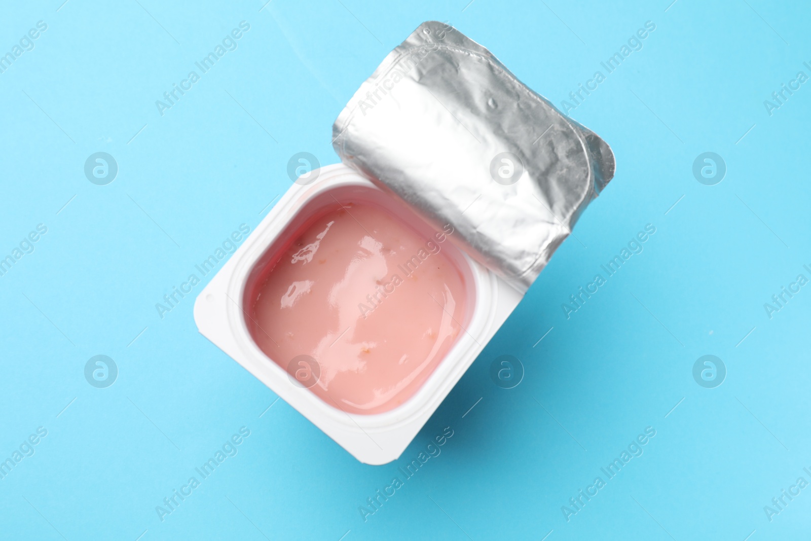 Photo of Delicious chocolate yogurt in plastic cup on light blue background, top view