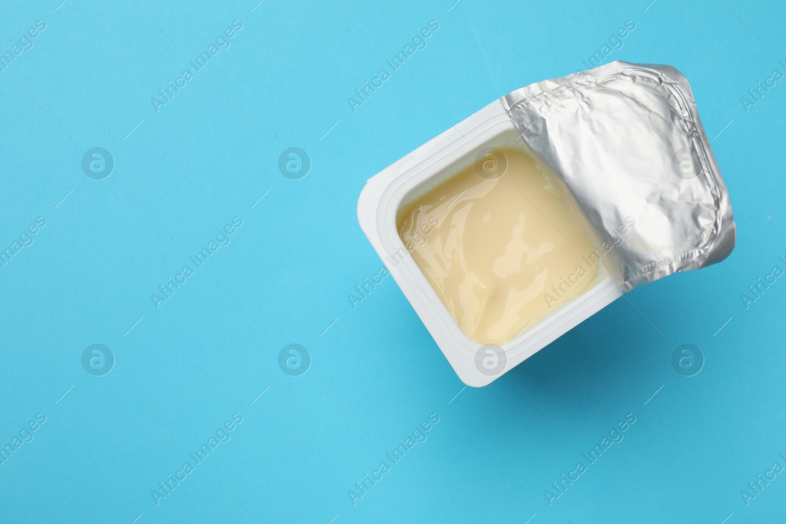 Photo of Delicious chocolate yogurt in plastic cup on light blue background, top view. Space for text