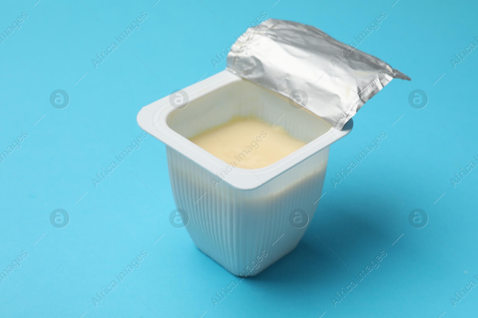 Photo of Delicious chocolate yogurt in plastic cup on light blue background, closeup