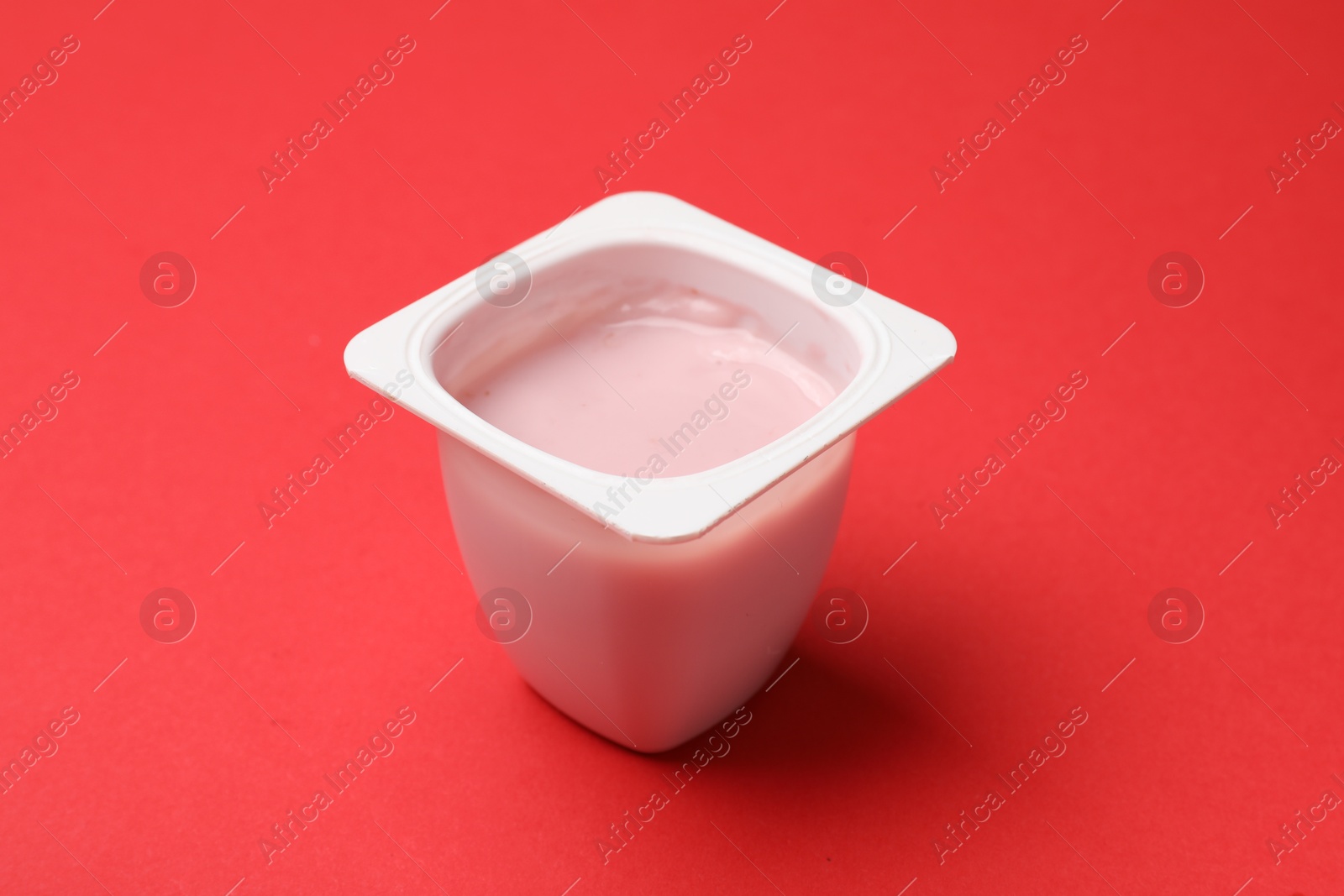 Photo of Delicious yogurt in plastic cup on red background, closeup