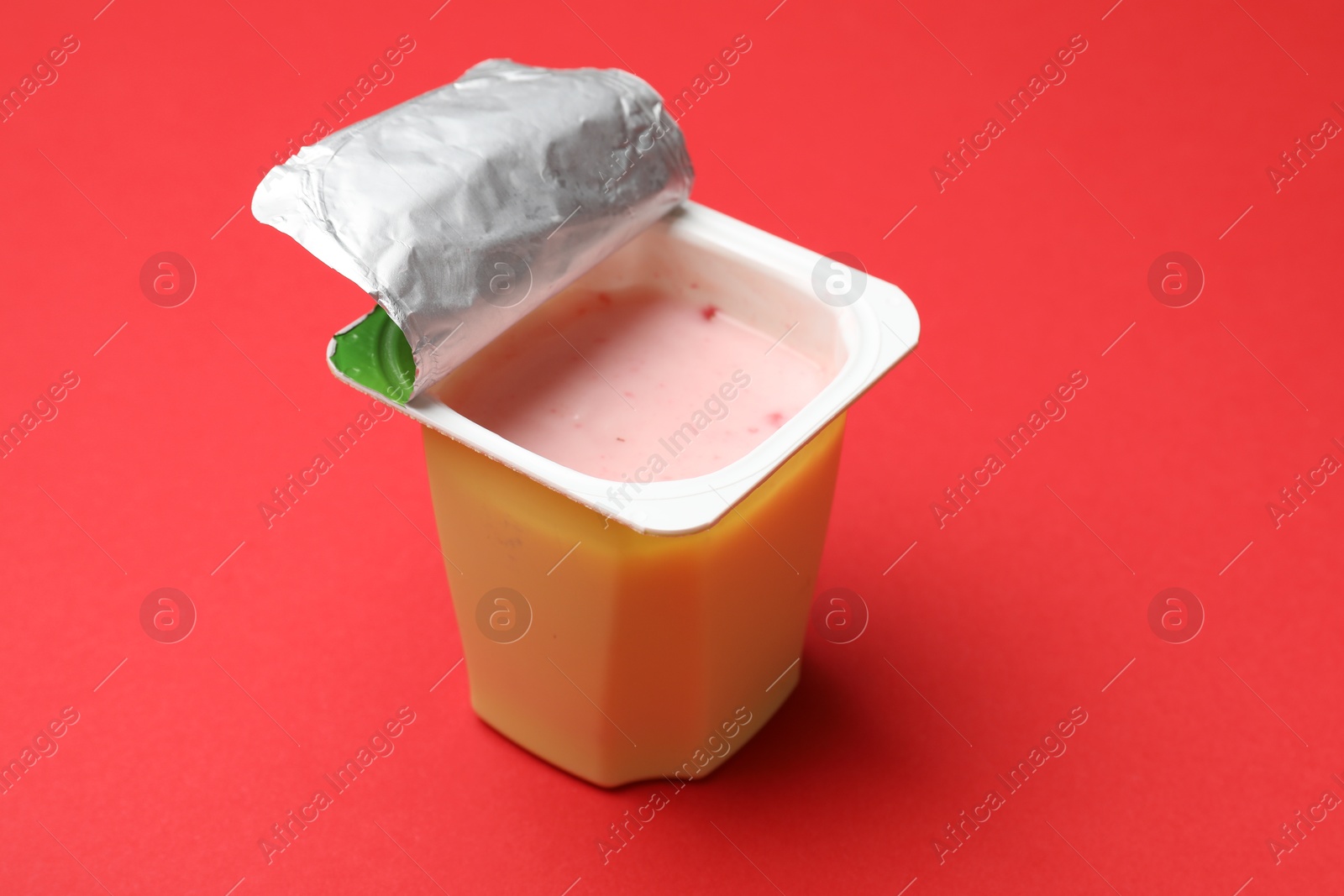 Photo of Delicious yogurt in plastic cup on red background, closeup