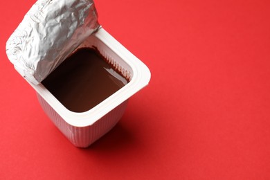 Photo of Delicious chocolate yogurt in plastic cup on red background, closeup. Space for text