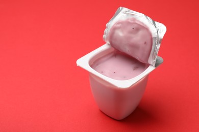 Photo of Delicious yogurt in plastic cup on red background, closeup. Space for text