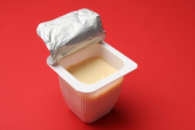 Photo of Delicious yogurt in plastic cup on red background, closeup