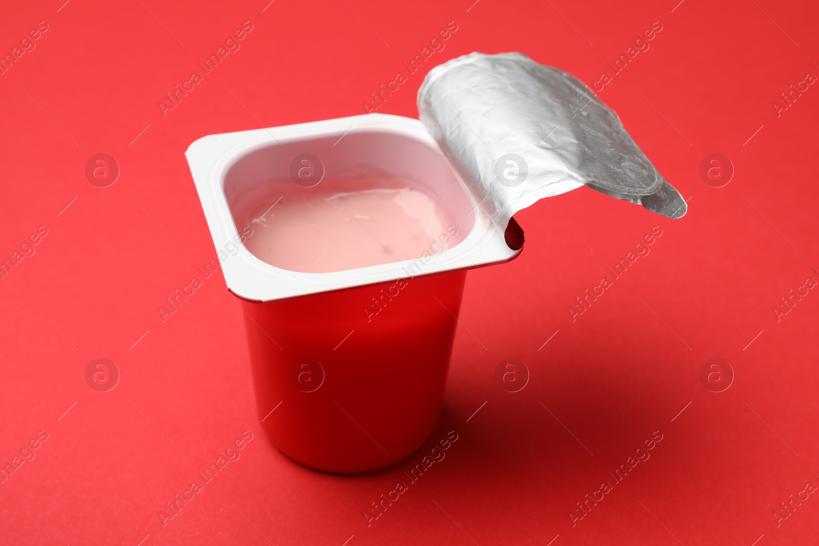 Photo of Delicious yogurt in plastic cup on red background, closeup