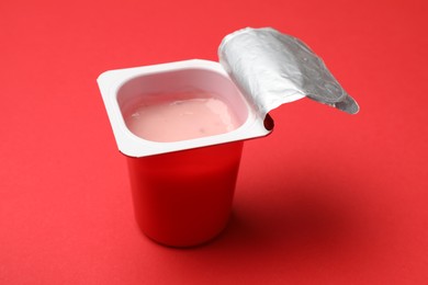 Photo of Delicious yogurt in plastic cup on red background, closeup