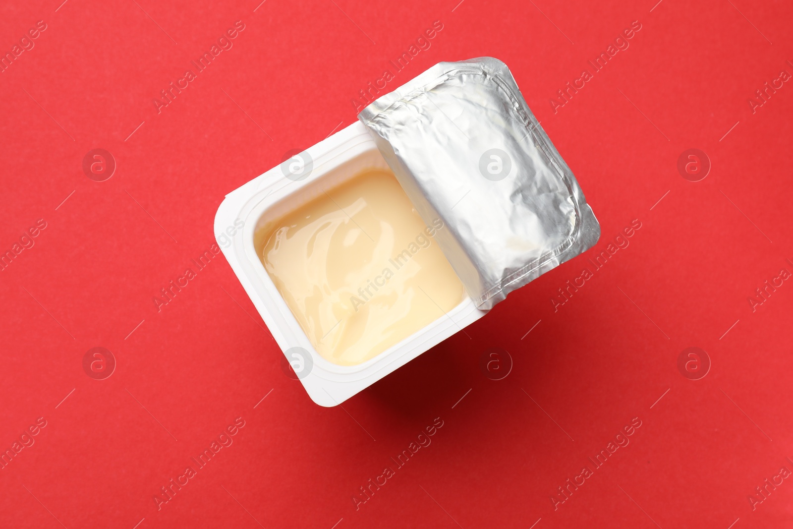 Photo of Delicious yogurt in plastic cup on red background, top view