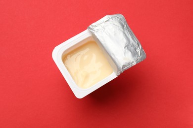 Photo of Delicious yogurt in plastic cup on red background, top view