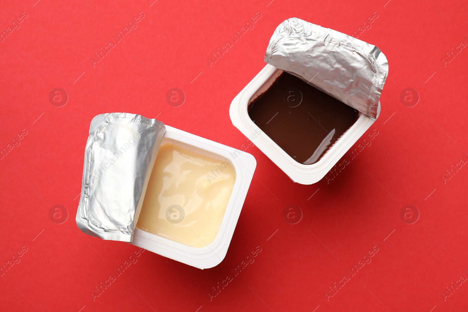 Photo of Delicious yogurts in plastic cups on red background, flat lay