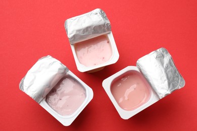 Photo of Delicious yogurts in plastic cups on red background, flat lay