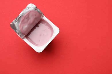 Photo of Delicious yogurt in plastic cup on red background, top view. Space for text