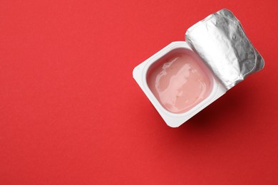 Photo of Delicious yogurt in plastic cup on red background, top view. Space for text