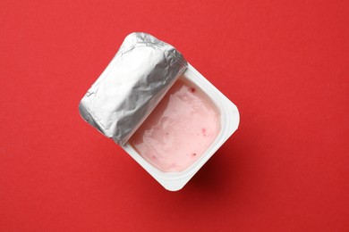 Photo of Delicious yogurt in plastic cup on red background, top view. Space for text