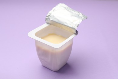 Photo of Delicious yogurt in plastic cup on violet background, closeup