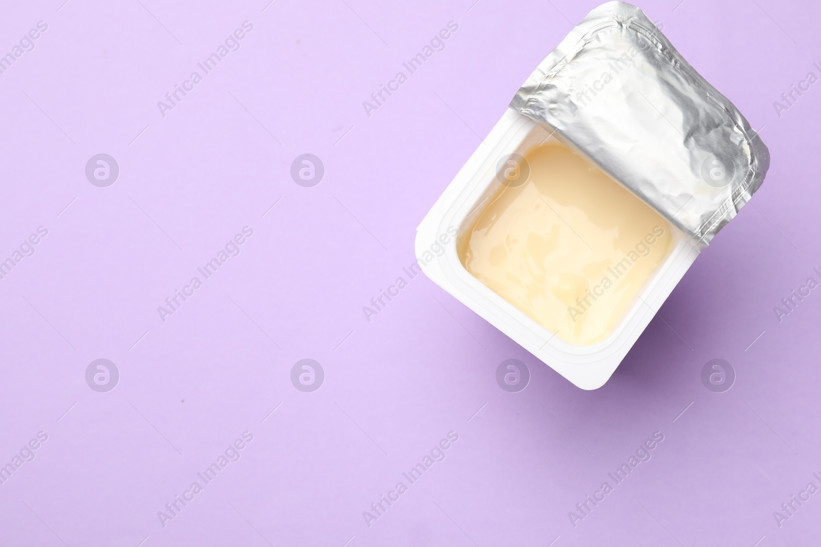 Photo of Delicious yogurt in plastic cup on violet background, top view. Space for text