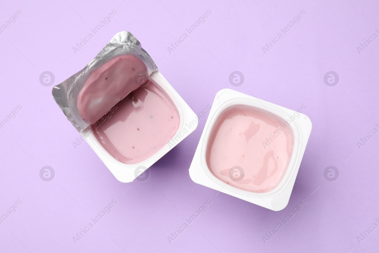 Photo of Delicious yogurts in plastic cups on violet background, flat lay