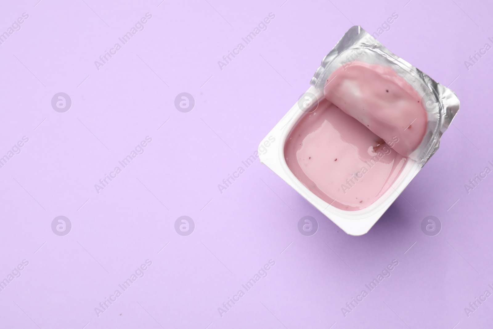 Photo of Delicious yogurt in plastic cup on violet background, top view. Space for text