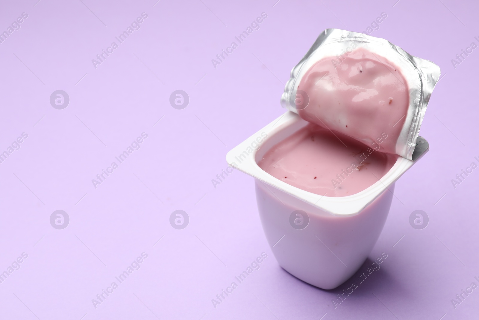 Photo of Delicious yogurt in plastic cup on violet background, closeup. Space for text