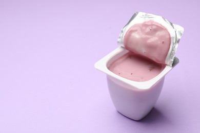 Photo of Delicious yogurt in plastic cup on violet background, closeup. Space for text