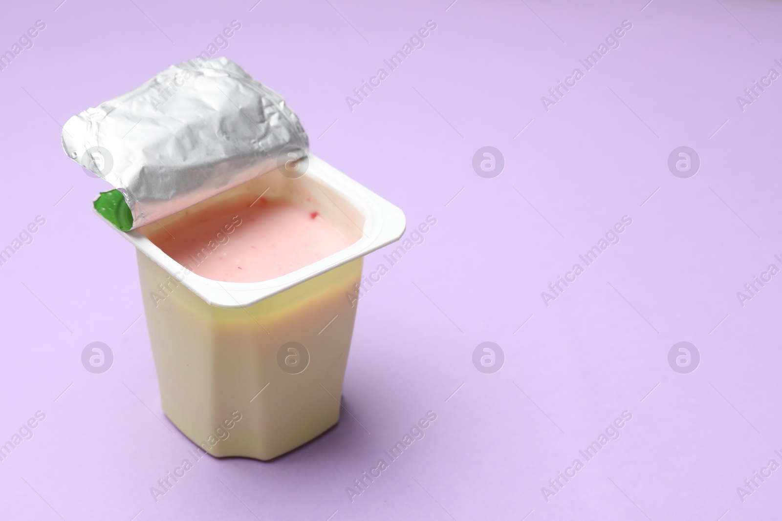 Photo of Delicious yogurt in plastic cup on violet background, closeup. Space for text