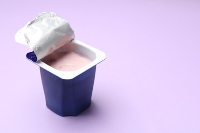 Photo of Delicious yogurt in plastic cup on violet background, closeup. Space for text