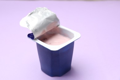 Photo of Delicious yogurt in plastic cup on violet background, closeup