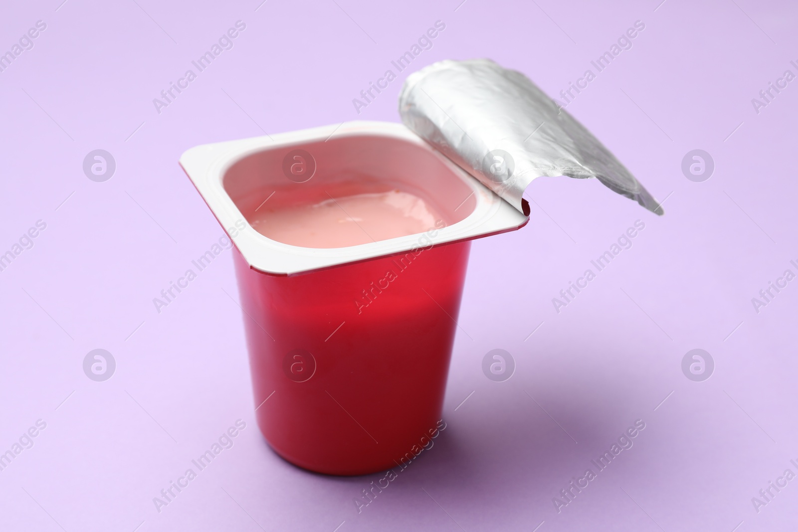 Photo of Delicious yogurt in plastic cup on violet background, closeup