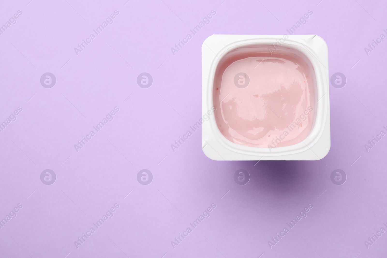 Photo of Delicious yogurt in plastic cup on violet background, top view. Space for text