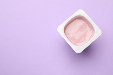 Photo of Delicious yogurt in plastic cup on violet background, top view. Space for text