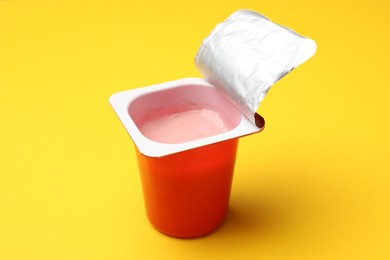 Photo of Delicious yogurt in plastic cup on yellow background, closeup