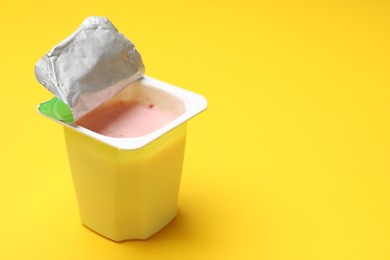 Photo of Delicious yogurt in plastic cup on yellow background, closeup. Space for text