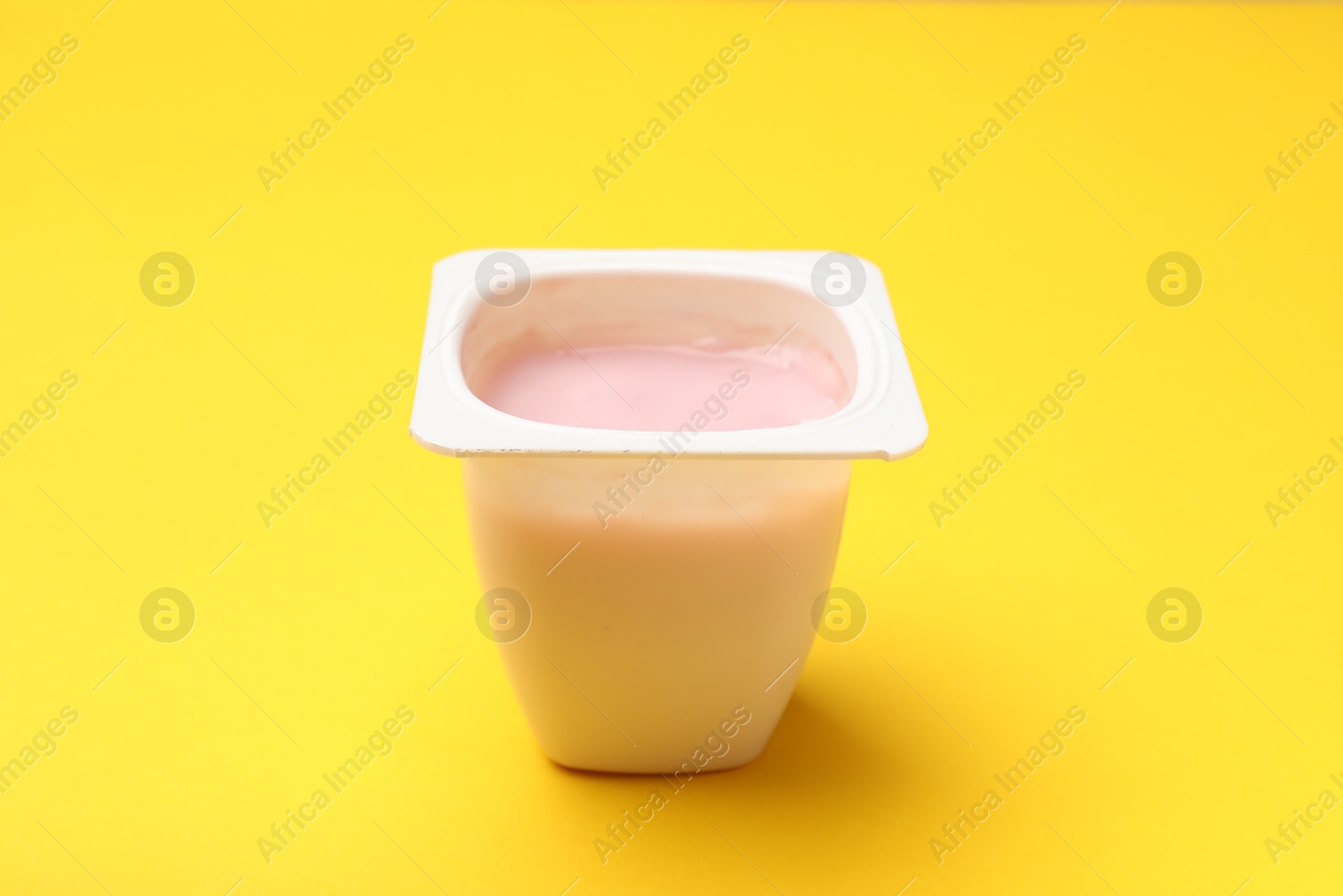 Photo of Delicious yogurt in plastic cup on yellow background, closeup