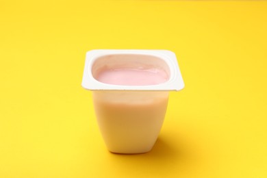 Photo of Delicious yogurt in plastic cup on yellow background, closeup