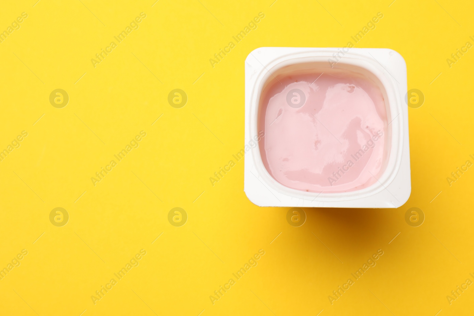 Photo of Delicious yogurt in plastic cup on yellow background, top view. Space for text