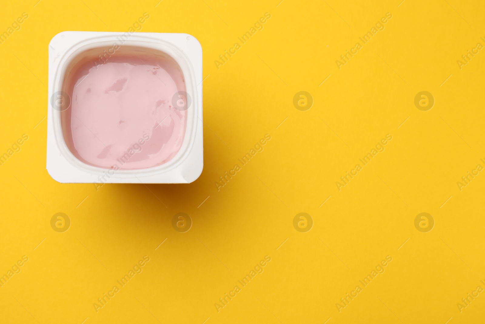 Photo of Delicious yogurt in plastic cup on yellow background, top view. Space for text