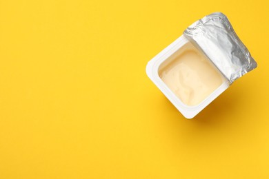 Photo of Delicious yogurt in plastic cup on yellow background, top view. Space for text