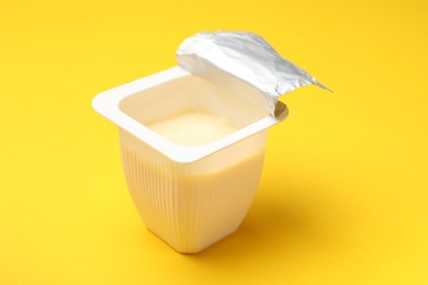 Photo of Delicious yogurt in plastic cup on yellow background, closeup