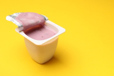 Photo of Delicious yogurt in plastic cup on yellow background, closeup. Space for text