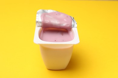 Photo of Delicious yogurt in plastic cup on yellow background, closeup