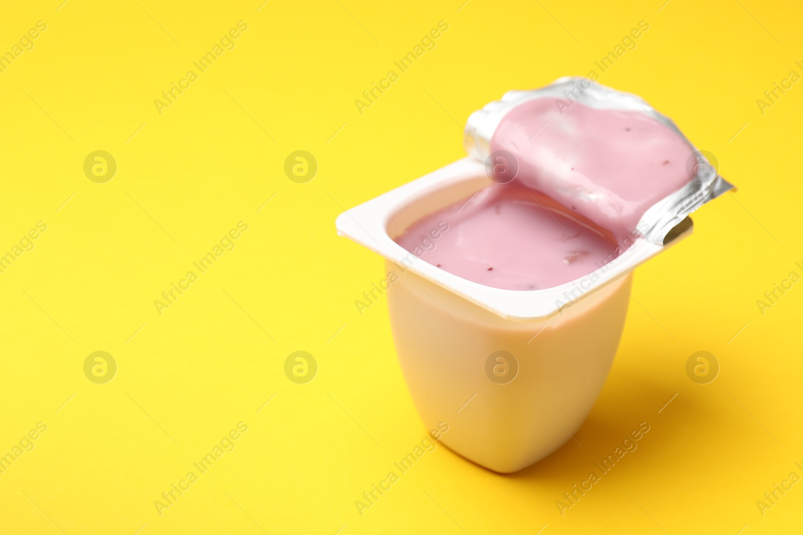 Photo of Delicious yogurt in plastic cup on yellow background, closeup. Space for text